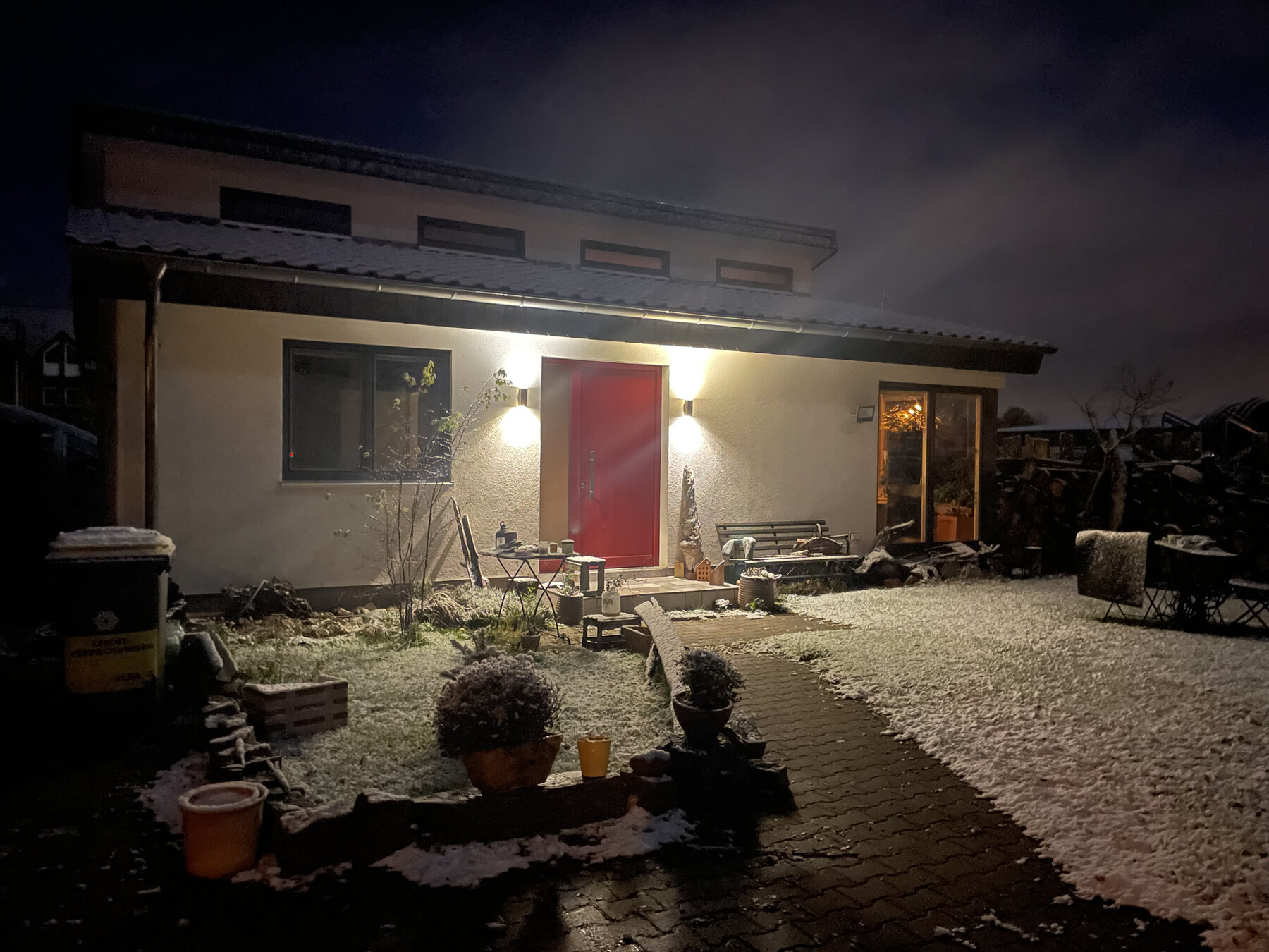 Hausansicht in der Abenddämmerung mit Schnee und beleuchteter Eingangstür